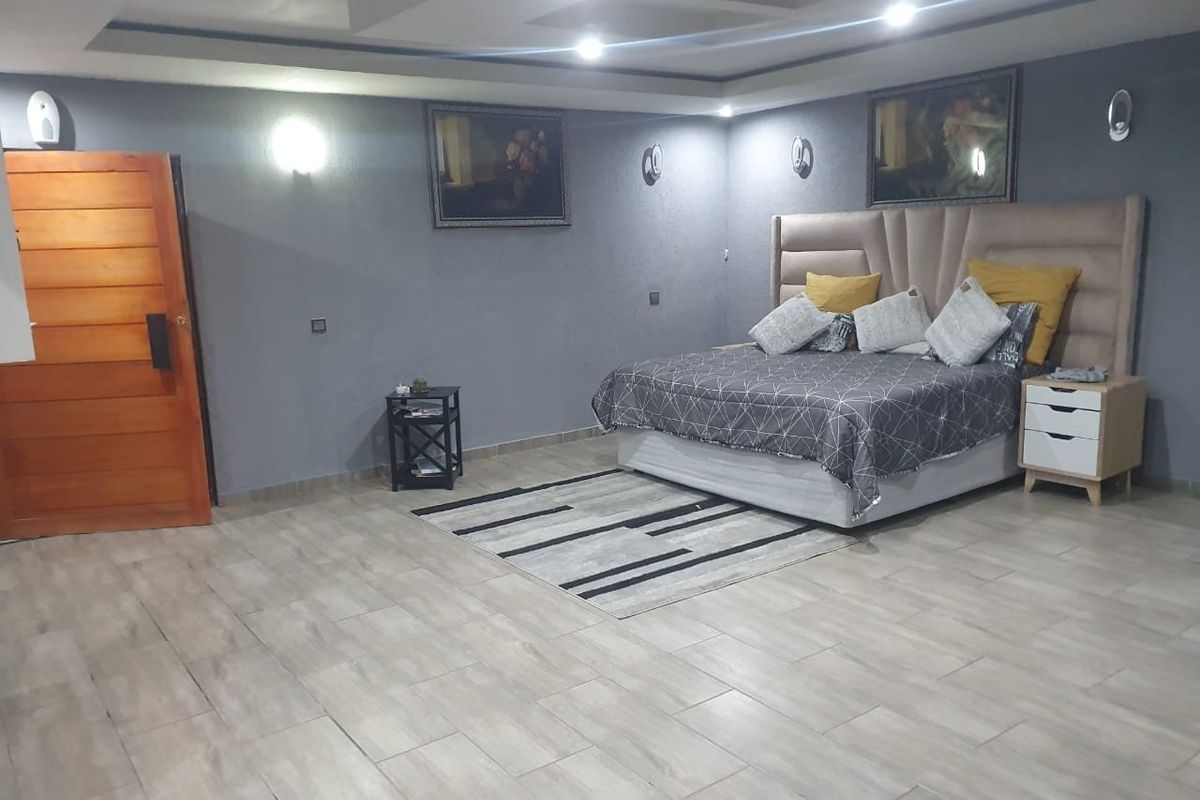 Spacious bedroom featuring modern tiled flooring, recessed ceiling lighting, and wall sconces, providing a comfortable and well-lit sleeping environment.