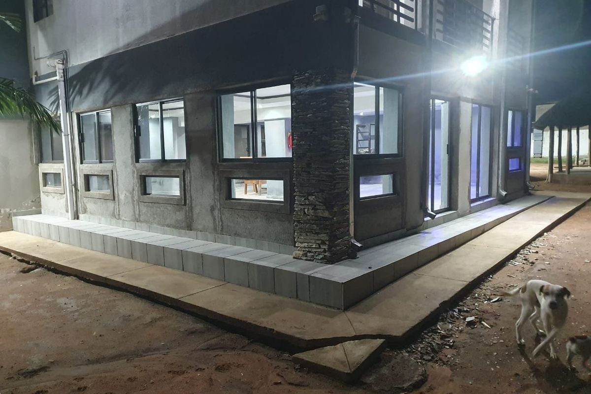 Night view of the property exterior featuring a tiled patio, stone-clad pillar, and large sliding glass windows and doors.