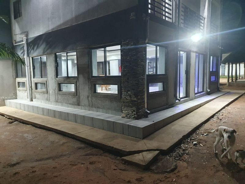 Night view of the property exterior featuring a tiled patio, stone-clad pillar, and large sliding glass windows and doors.