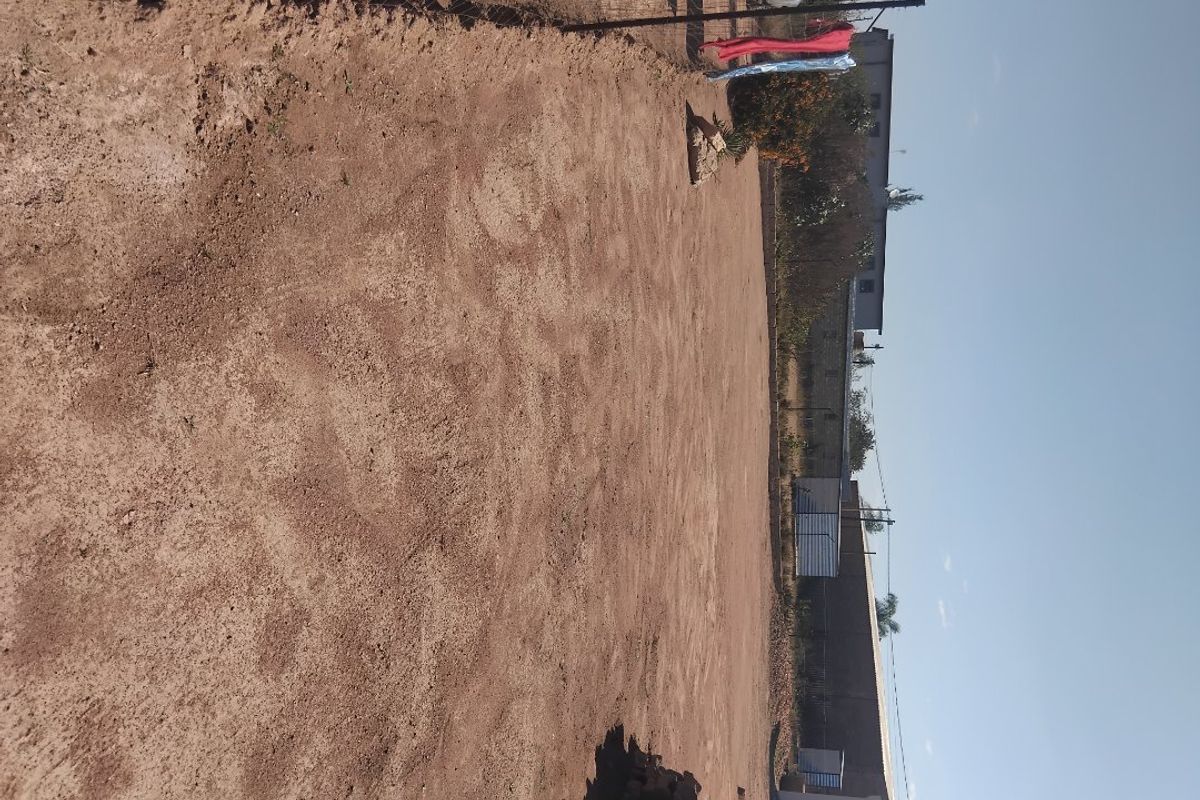 A large, undeveloped outdoor space featuring bare earth, enclosed by a wire fence and boundary wall, offering potential for landscaping.