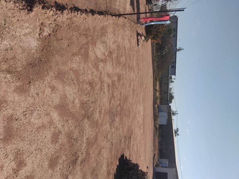 A large, undeveloped outdoor space featuring bare earth, enclosed by a wire fence and boundary wall, offering potential for landscaping.
