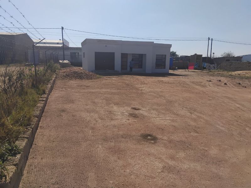 Front view of a single-story house featuring a garage and an expansive, unpaved yard area enclosed by perimeter fencing.