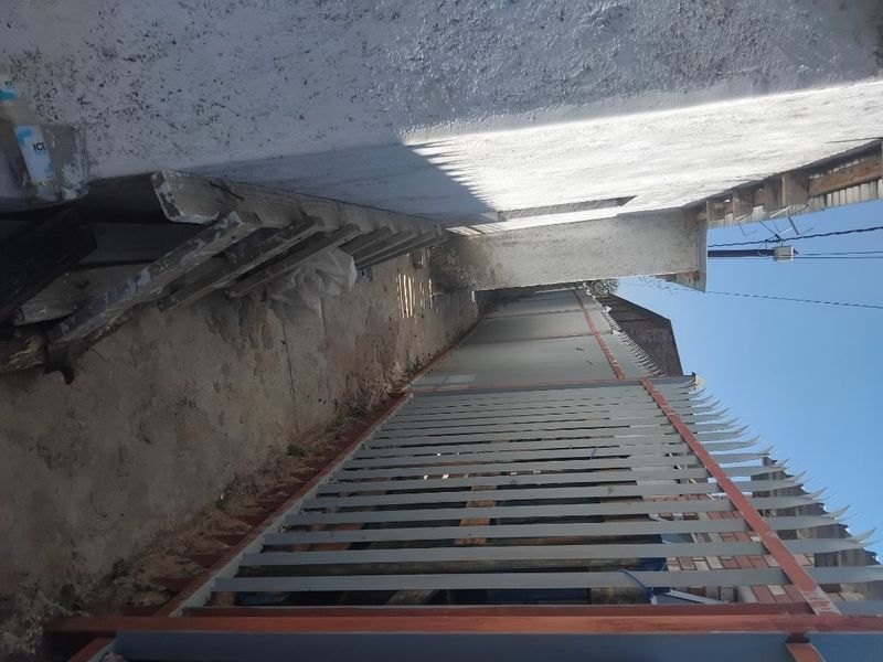A narrow side passage featuring a metal security fence with spiked topping and an unpaved ground surface.