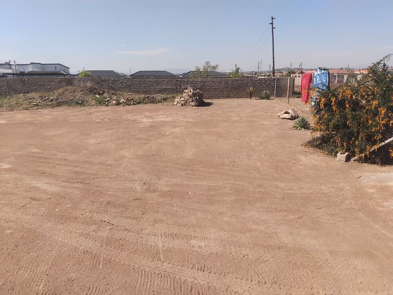 A large, undeveloped backyard area featuring a perimeter boundary wall and open, unlandscaped ground space.