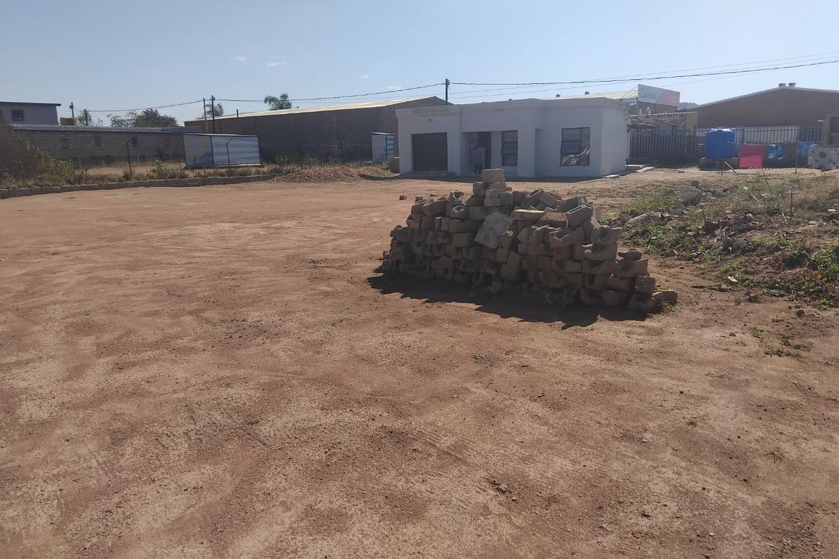 A view of a property exterior featuring an unpaved yard with building debris and a single-story structure in the background.