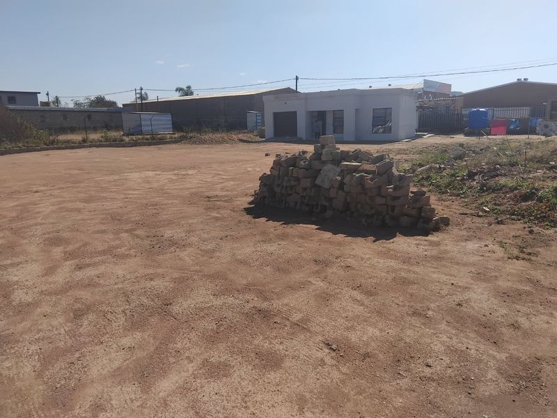 A view of a property exterior featuring an unpaved yard with building debris and a single-story structure in the background.