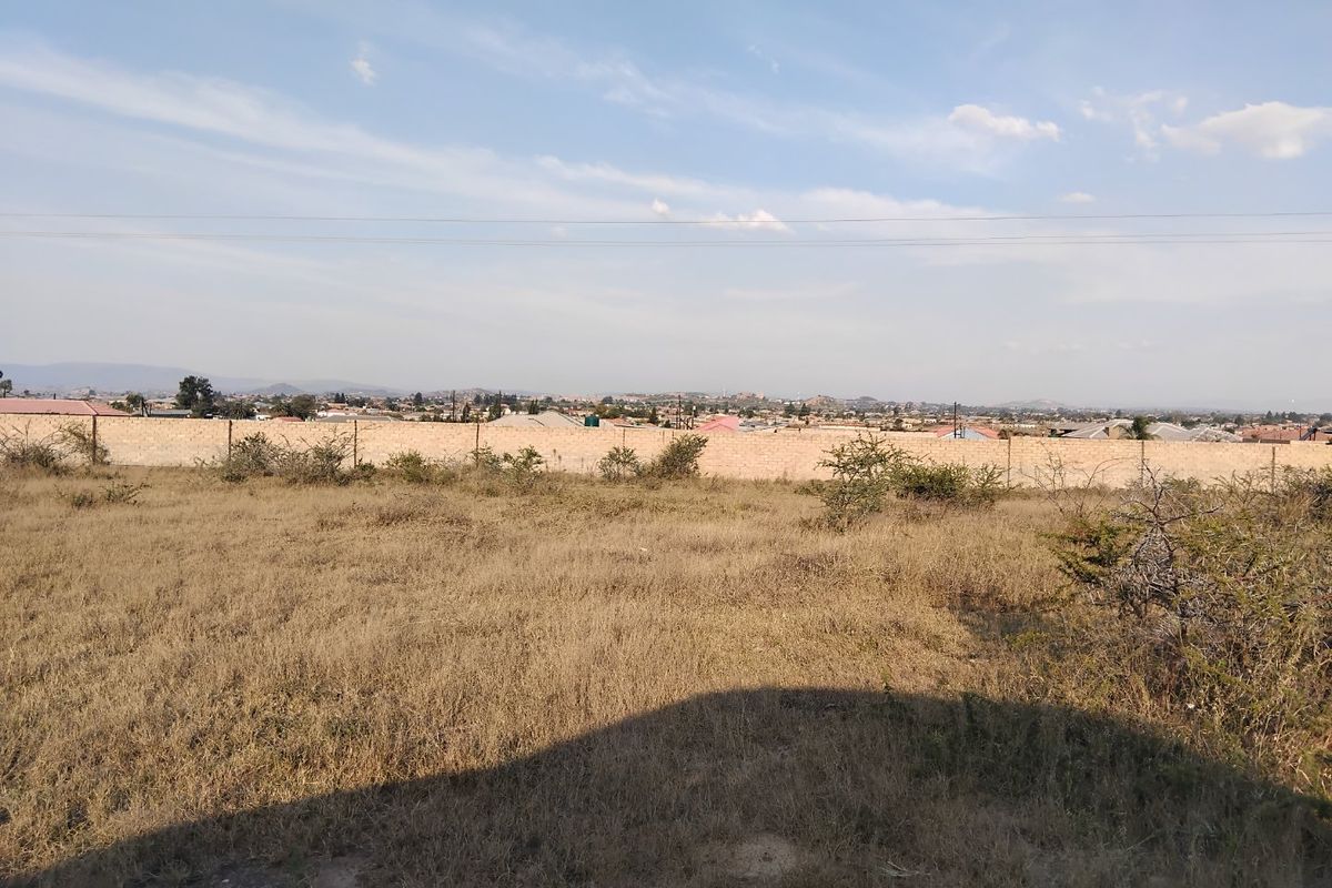 A view across the vacant residential land showing the perimeter boundary wall and surrounding neighborhood landscape.