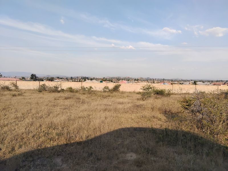 A view across the vacant residential land showing the perimeter boundary wall and surrounding neighborhood landscape.