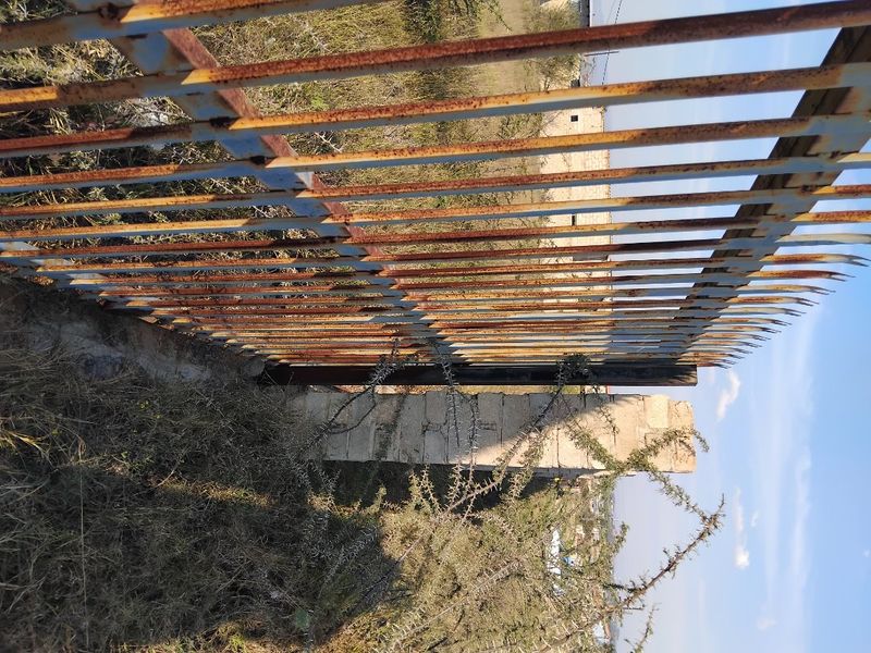 A view of a weathered metal security fence and concrete pillar on a vacant residential plot.