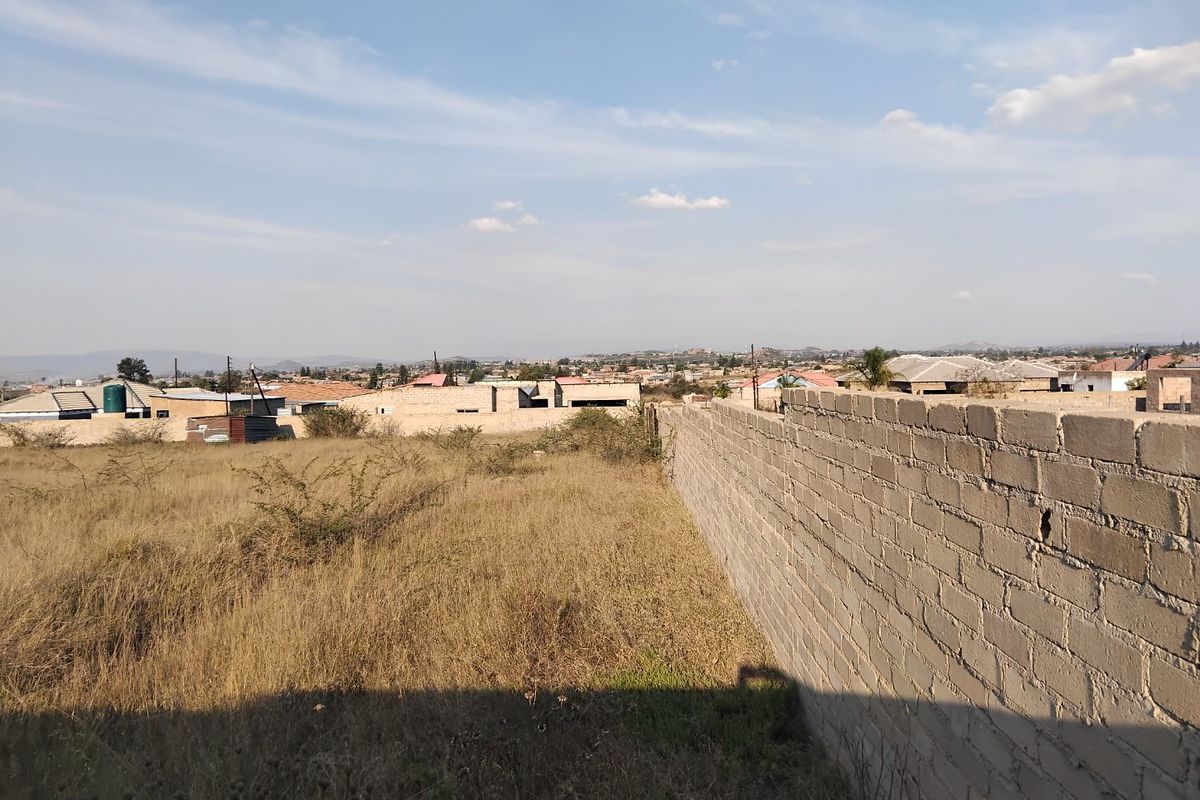 A view of a vacant residential plot featuring a perimeter brick wall and surrounding neighborhood landscape.