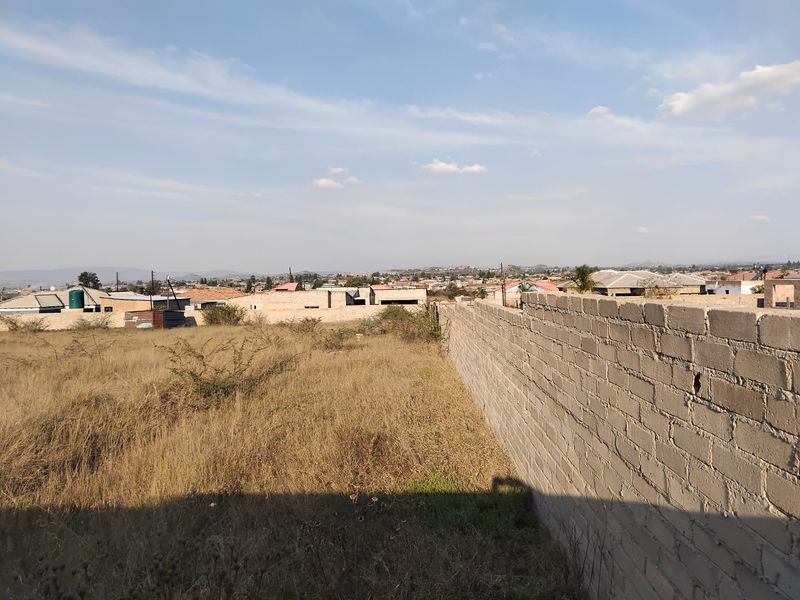 A view of a vacant residential plot featuring a perimeter brick wall and surrounding neighborhood landscape.