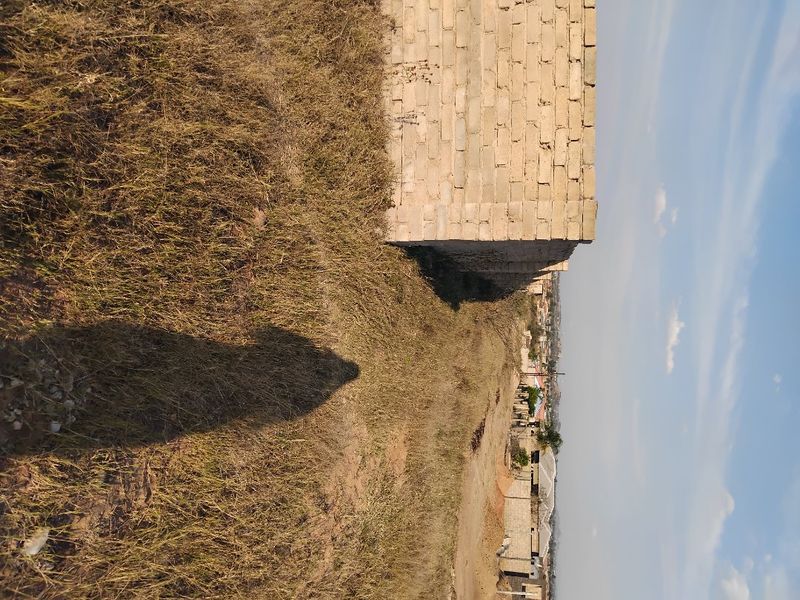 A view of a vacant residential plot featuring a partial boundary wall and natural grass terrain.