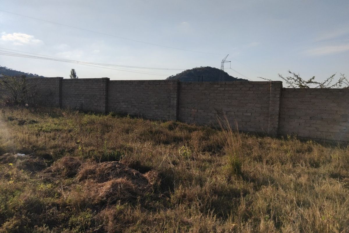 A vacant residential plot featuring a perimeter brick wall and natural, overgrown vegetation with distant mountain views.