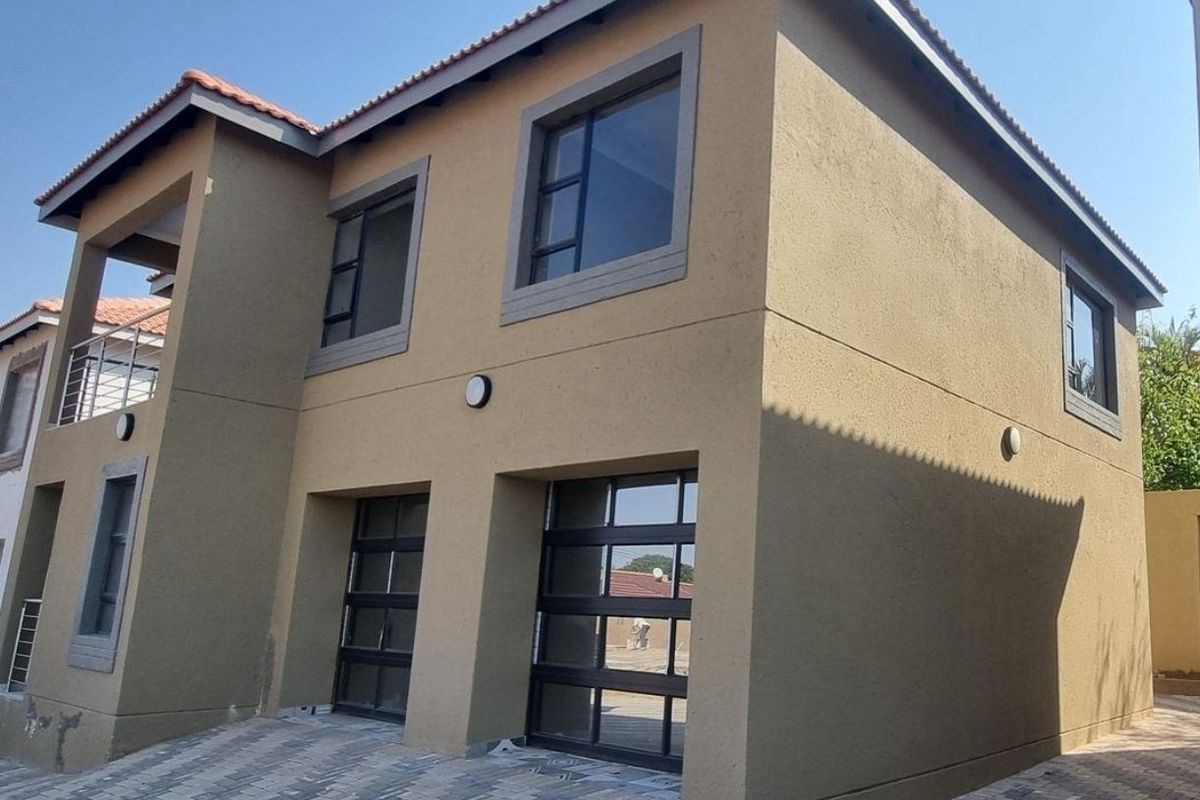 Front elevation of a double-story townhouse featuring a double garage, paved driveway, and an upper-level balcony with modern finishes.