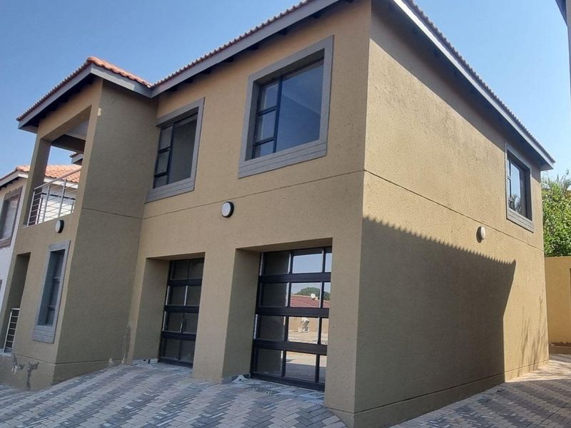 Front elevation of a double-story townhouse featuring a double garage, paved driveway, and an upper-level balcony with modern finishes.