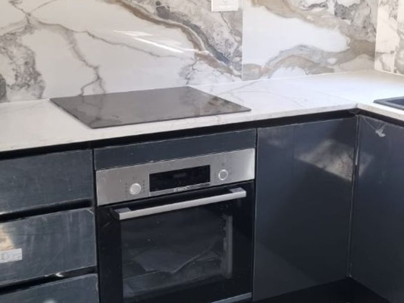 Modern kitchen featuring sleek grey cabinetry, stone countertops, a marble-look splashback, and integrated Bosch oven and electric hob.