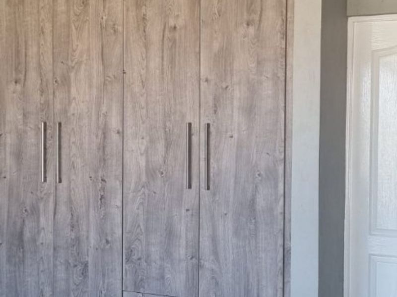A clean bedroom interior featuring modern wood-look built-in cupboards, neutral grey tiled flooring, and classic ceiling coving.