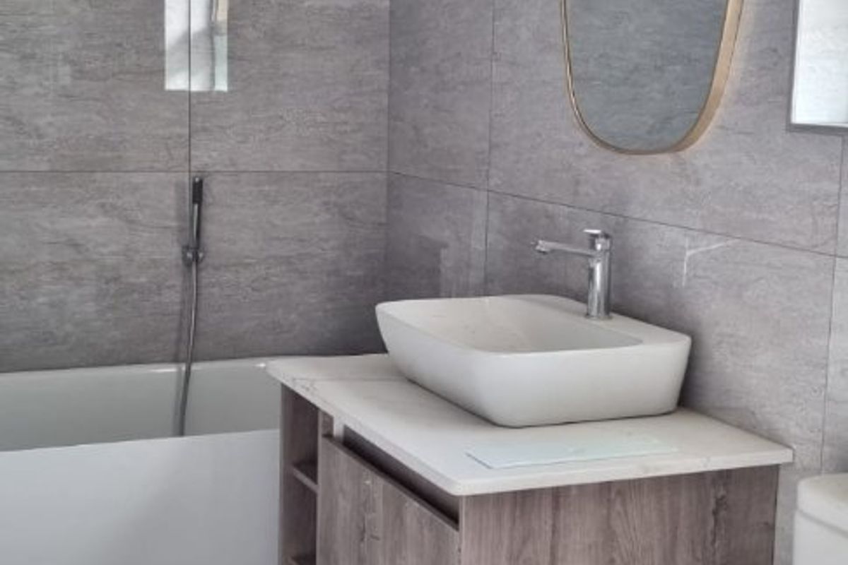 Modern bathroom featuring grey stone-look wall and floor tiles, a vessel sink vanity, and a built-in bathtub with a sleek chrome hand shower.