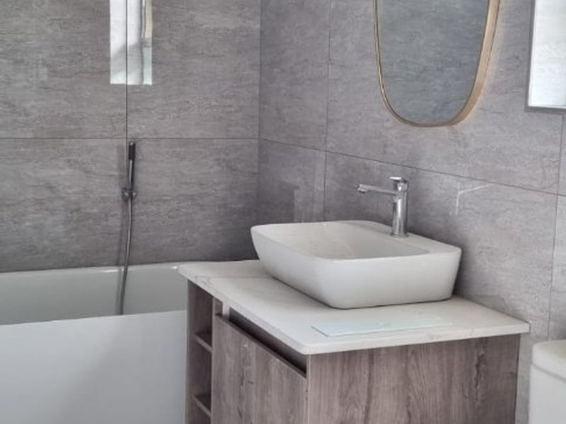 Modern bathroom featuring grey stone-look wall and floor tiles, a vessel sink vanity, and a built-in bathtub with a sleek chrome hand shower.