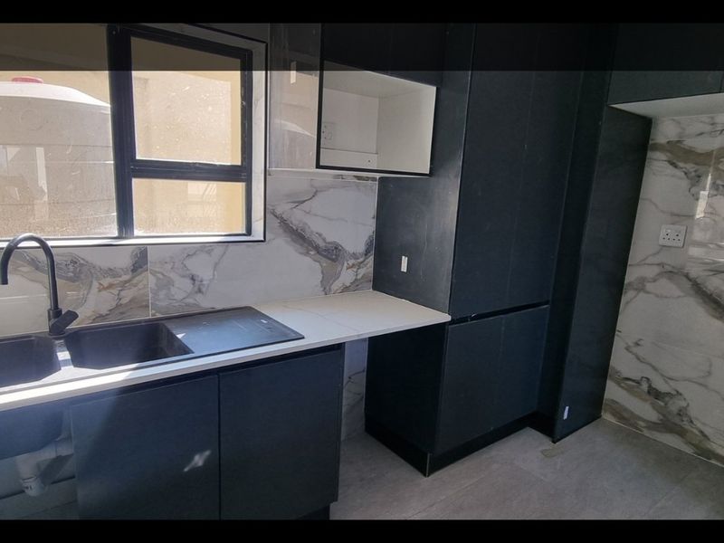 Modern kitchen featuring dark cabinetry, marble-look splashback tiles, stone countertops, and a double sink with a black mixer tap.