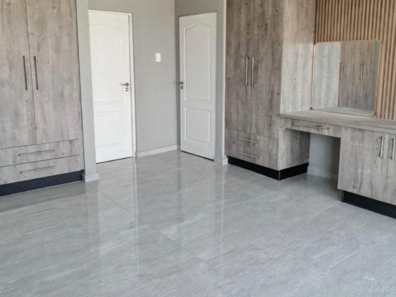 A modern, empty bedroom featuring extensive built-in cupboards, a matching vanity unit, sleek tiled flooring, and decorative slatted wood wall paneling.