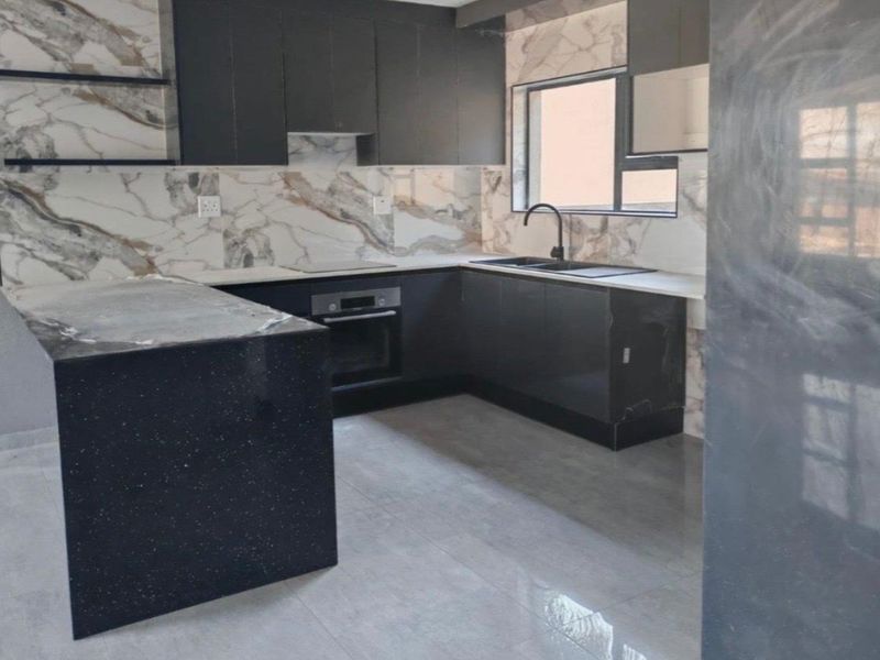 Modern kitchen featuring dark cabinetry, marble-look splashbacks, stone countertops, a central island, and integrated appliances with a sleek, contemporary finish.