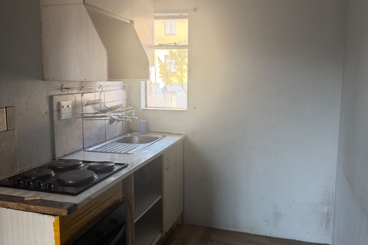 A compact kitchen featuring built-in cabinetry, an electric hob, and an oven, with tiled flooring and a window providing natural light.