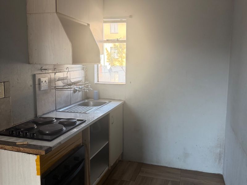 A compact kitchen featuring built-in cabinetry, an electric hob, and an oven, with tiled flooring and a window providing natural light.