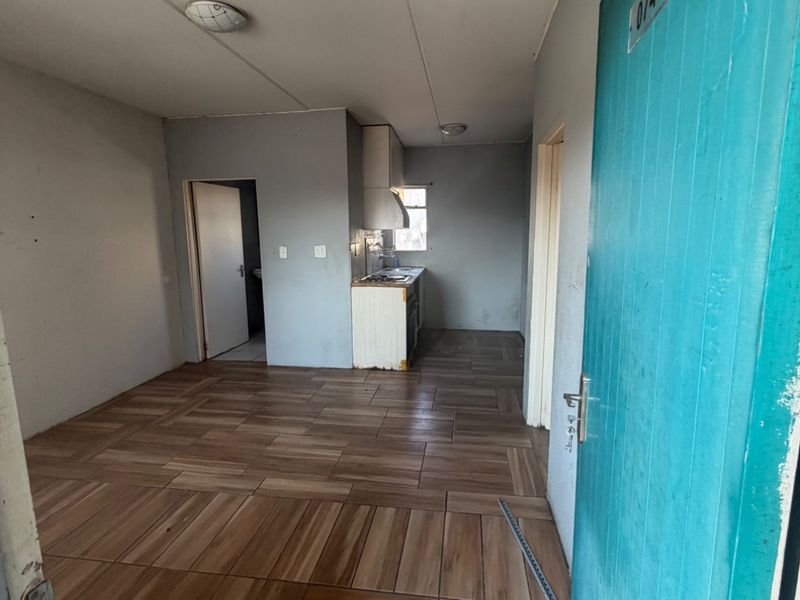 An open-plan living and kitchen area featuring wood-look tiled flooring, built-in cabinetry, and a functional layout, presenting a blank canvas for renovation.