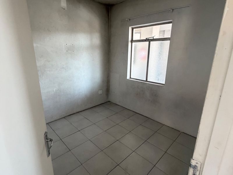 An empty bedroom featuring tiled flooring and a single window, requiring cosmetic updates to the walls and ceiling.