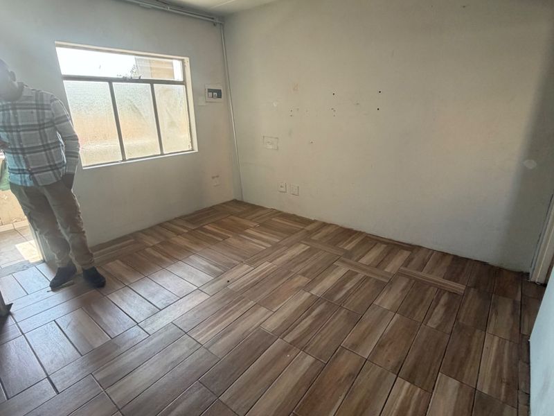 An empty bedroom featuring wood-look tiled flooring, a single window, and surface-mounted electrical conduit, presenting a blank canvas for interior design.