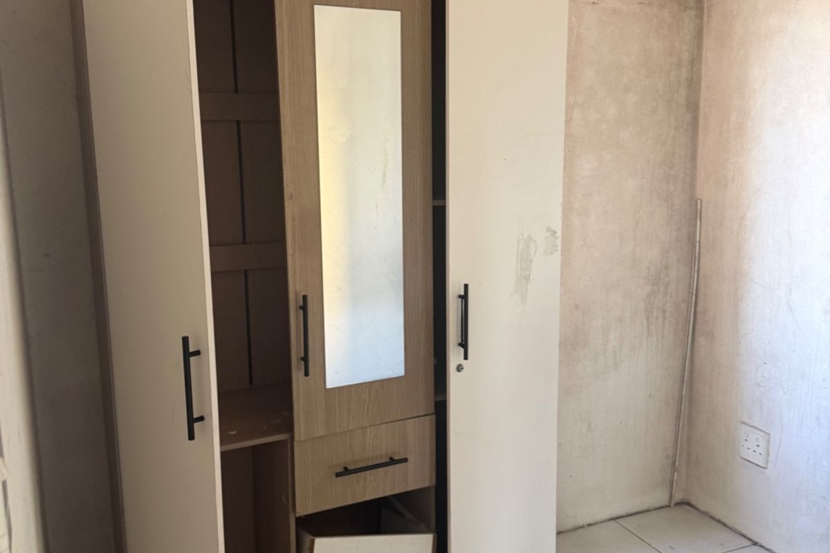 A bedroom space featuring tiled flooring and unfinished wall surfaces, currently containing a damaged wardrobe unit.