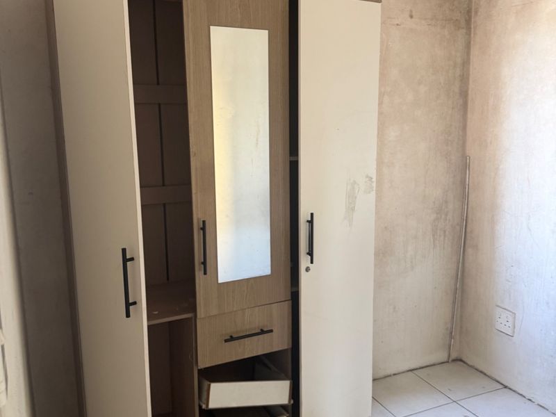 A bedroom space featuring tiled flooring and unfinished wall surfaces, currently containing a damaged wardrobe unit.