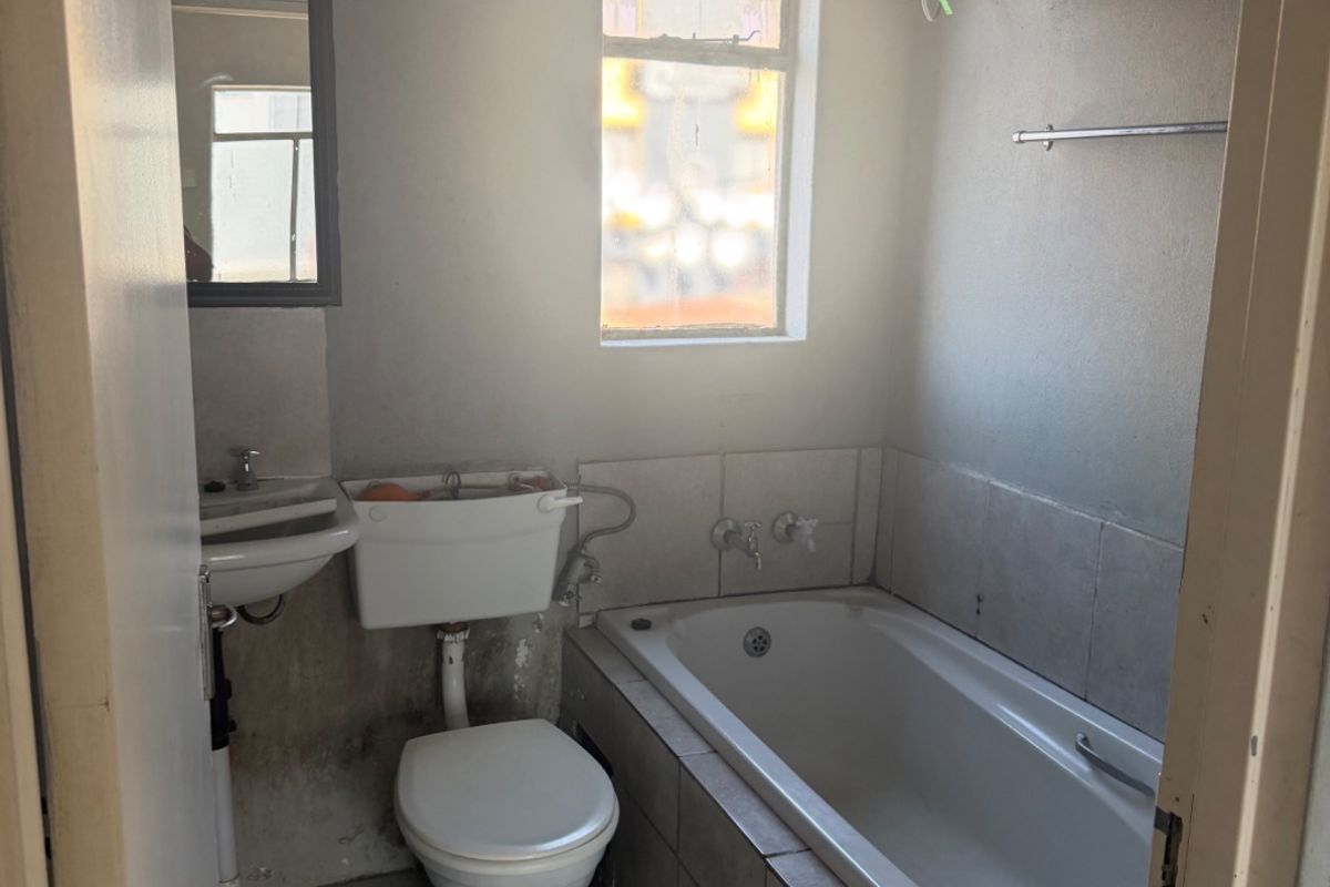 A dated bathroom featuring a standard bathtub, toilet, and pedestal basin with tiled finishes, requiring significant cosmetic updates and maintenance.