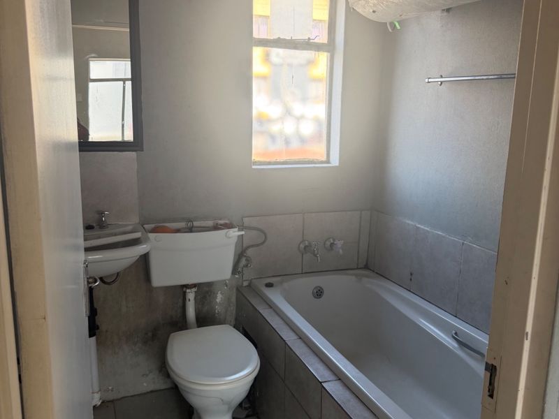 A dated bathroom featuring a standard bathtub, toilet, and pedestal basin with tiled finishes, requiring significant cosmetic updates and maintenance.