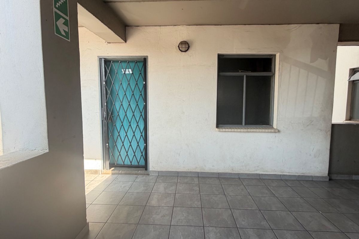 A covered apartment building corridor featuring tiled flooring, a security gate, and an external wall light.