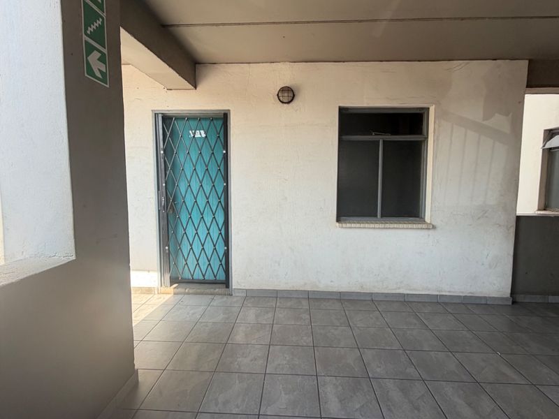 A covered apartment building corridor featuring tiled flooring, a security gate, and an external wall light.