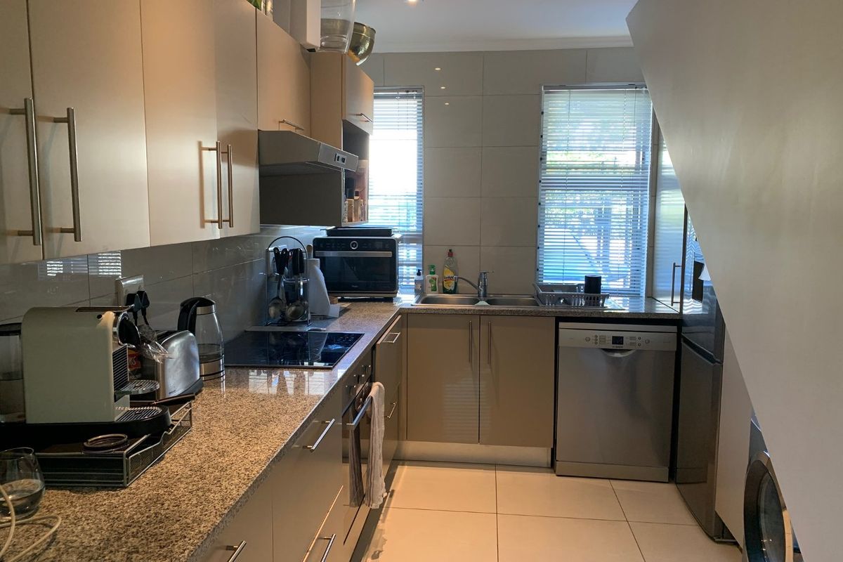 A functional kitchen featuring granite countertops, built-in cabinetry, an electric hob, and integrated appliances, finished with neutral wall and floor tiles.