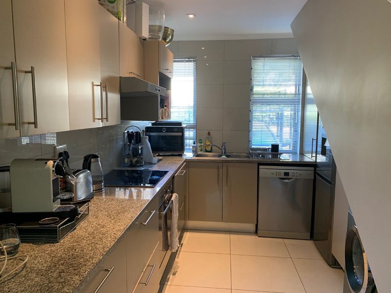 A functional kitchen featuring granite countertops, built-in cabinetry, an electric hob, and integrated appliances, finished with neutral wall and floor tiles.