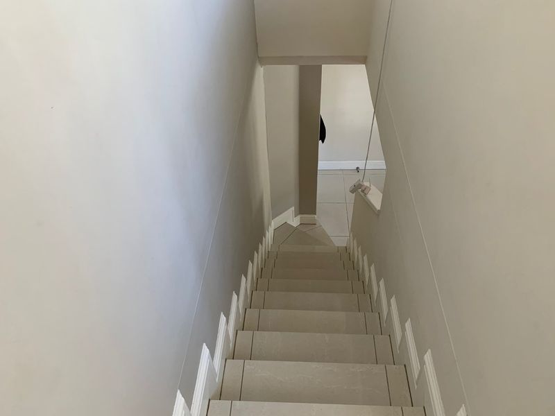 A view looking down a tiled staircase in an apartment, featuring neutral wall finishes and skirting boards.