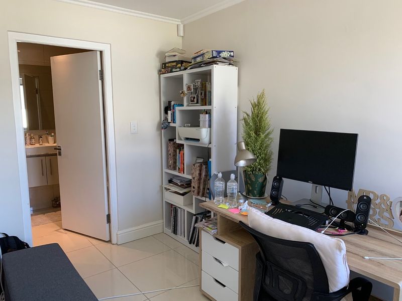 A bedroom space featuring tiled flooring and an adjoining bathroom, currently utilized as a home office area.