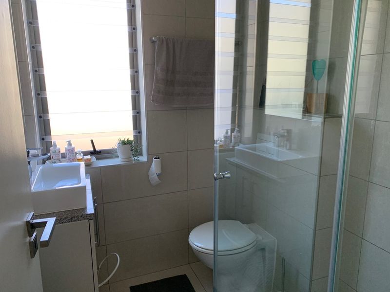 Modern bathroom featuring a vessel sink on a granite vanity, a wall-mounted toilet, and a glass-enclosed shower with neutral wall tiling.