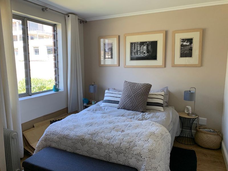 A well-maintained bedroom featuring laminate flooring, neutral wall tones, and a large window providing natural light.