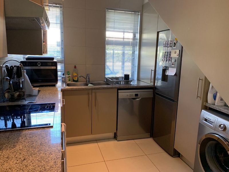 A functional kitchen featuring granite countertops, stainless steel appliances, built-in cabinetry, and tiled finishes, maximizing space under the staircase.