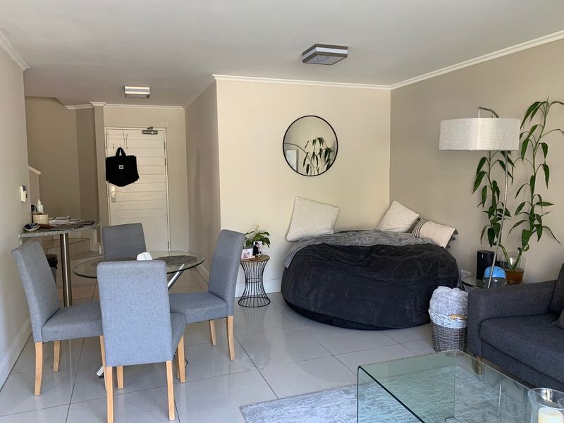An open-plan living area featuring polished tiled flooring, neutral wall tones, and a functional layout with direct access to the entrance.