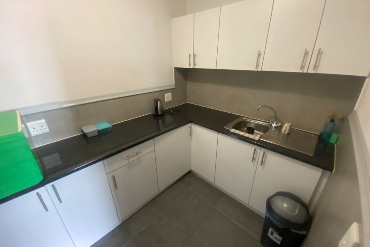 A compact, functional kitchen area featuring white built-in cabinetry, dark stone countertops, a stainless steel sink, and neutral tiled finishes.