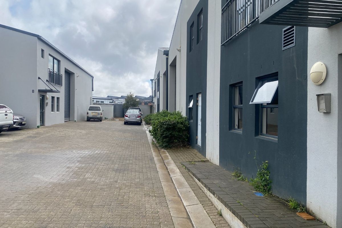 Exterior view of an industrial complex featuring a paved driveway, roller shutter access, and modern multi-story building facades.