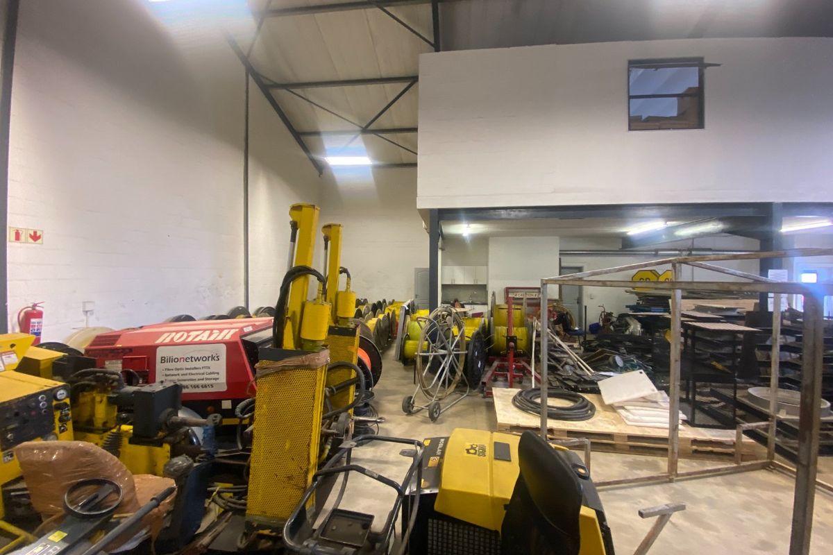 Spacious industrial utility area featuring high ceilings with exposed steel trusses, a mezzanine level, and durable concrete flooring suitable for storage or workshop use.