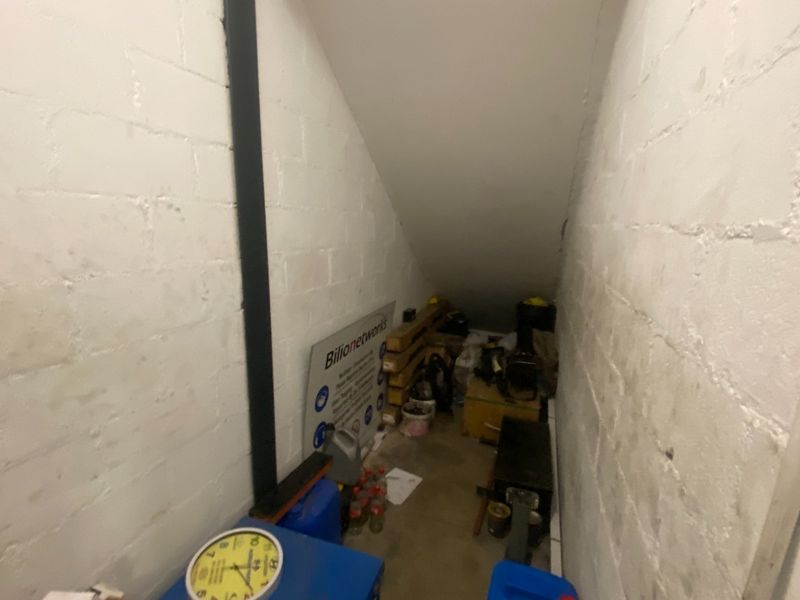 A small, sloped utility storage space under a staircase featuring painted brick walls and a concrete floor.