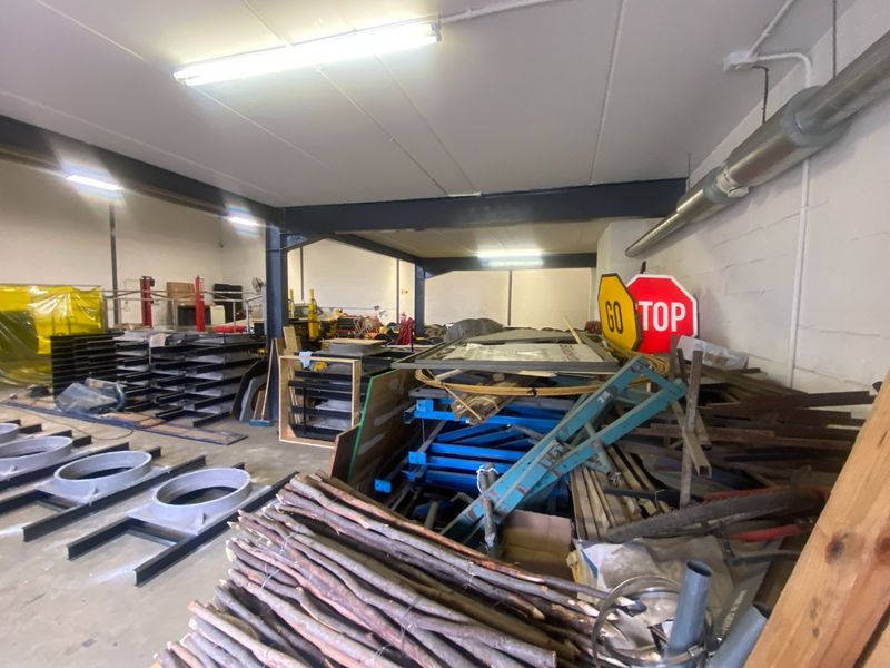 Industrial utility space featuring exposed steel structural beams, concrete flooring, and overhead fluorescent lighting, currently utilized for storage.